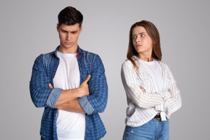 Angry young couple with crossed arms ignoring each other, symbolizing relationship troubles and lack of intimacy, on a gray background